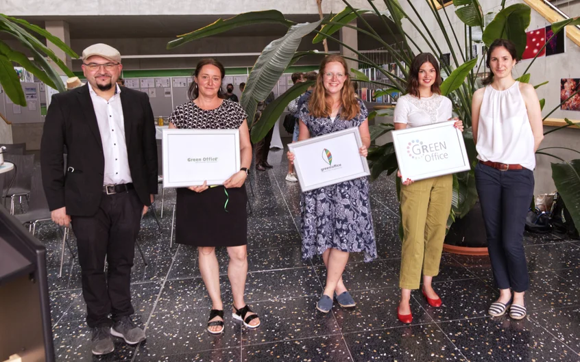 Gruppenfoto mit fünf Personen, die zum Teil gerahmte Ausdrucke von Logos in den Händen halten. (öffnet Vergrößerung des Bildes)