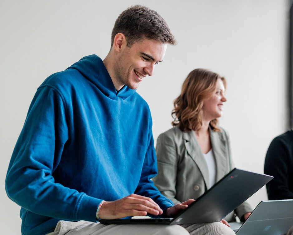 Ein Student und eine Studentin arbeiten lächelnd an ihren Laptops
