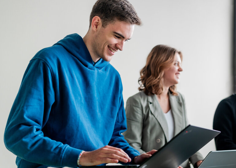 Ein Student und eine Studentin arbeiten lächelnd an ihren Laptops