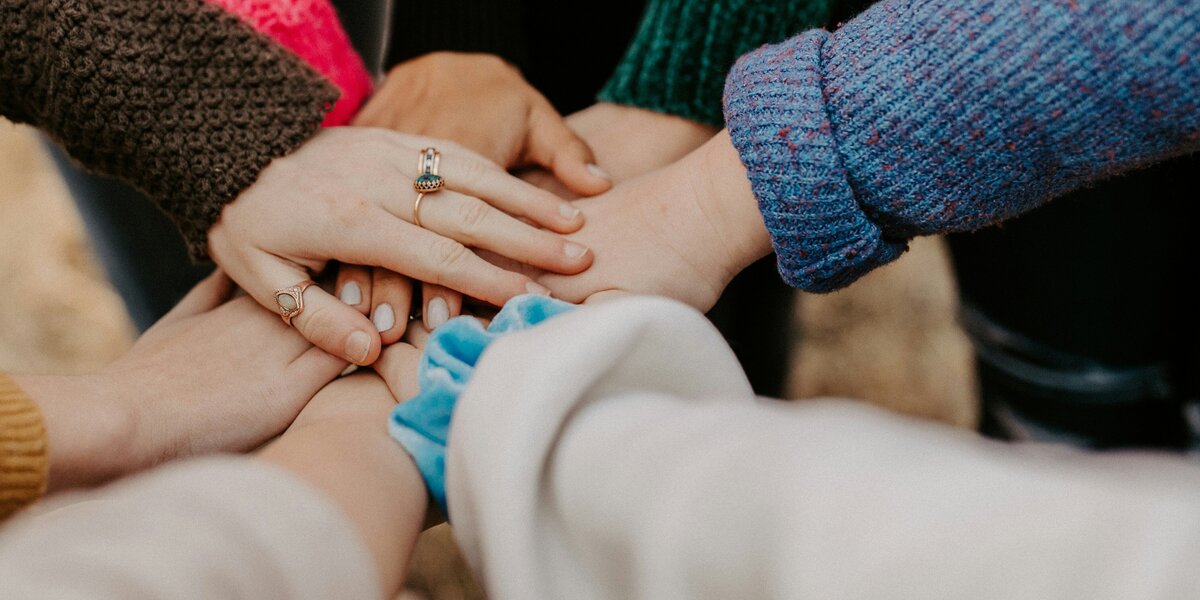 Zu sehen sind die Hände und Arme von verschiedenen Menschen, die ihre Hände aufeinander gelegt haben.