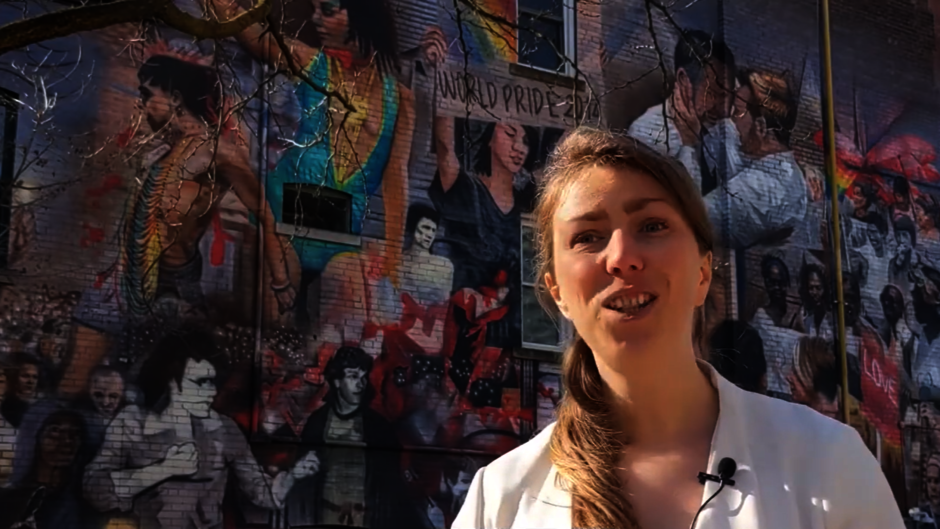 Frau mit Ansteckmikrofon vor Wand mit buntem Mural im Hintergrund.