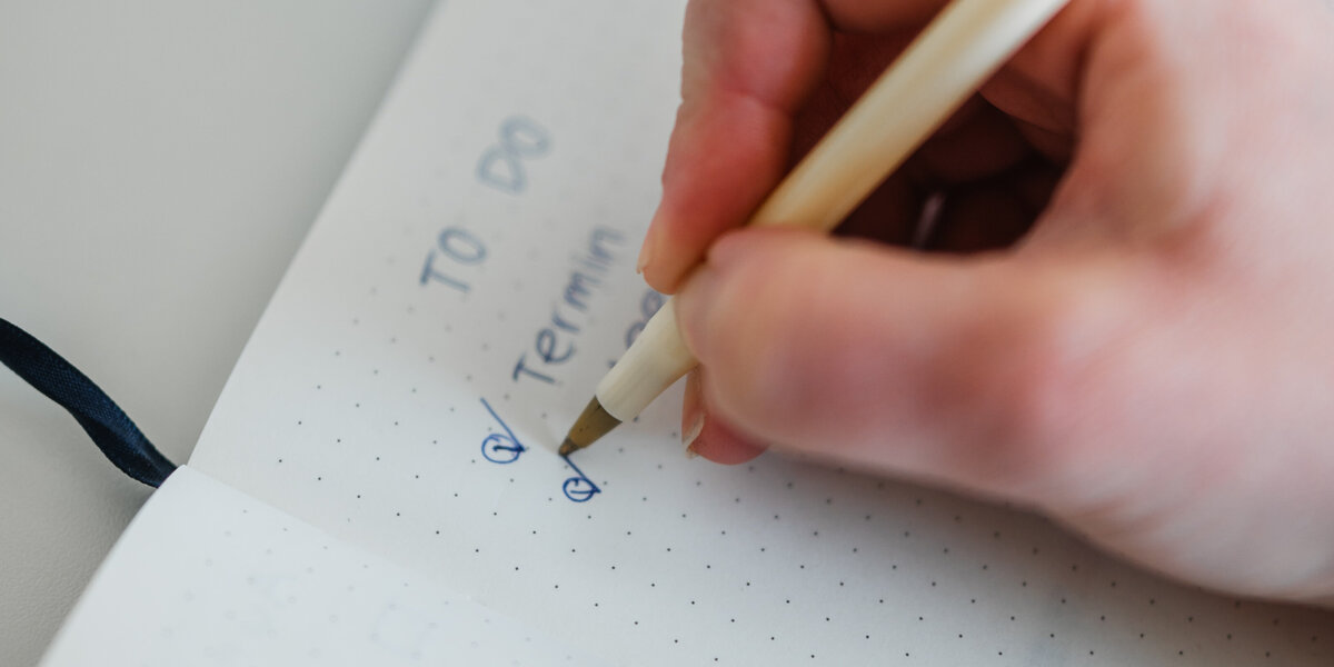 Person, die mit einem Stift einen Haken in ein Notizbuch macht.