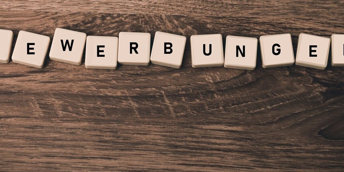 Man sieht einen Holztisch, auf dem Würfel liegen, die mit dem Wort Bewerbungen bedruckt sind