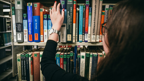 Eine Frau greift nach einem Buch in einem Bücherregal