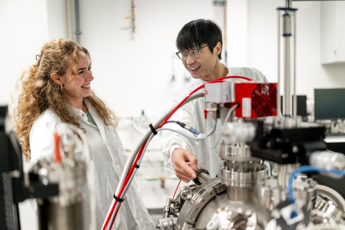 Zwei junge Forschende, die an einem Gerät stehen. (opens enlarged image)