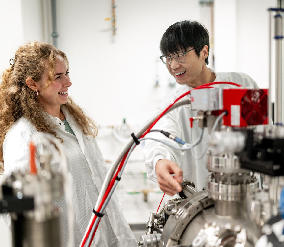 Zwei junge Forschende, die an einem Gerät stehen.