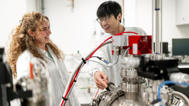 Zwei junge Forschende, die an einem Gerät stehen.