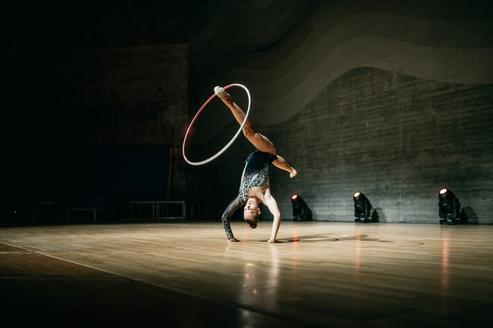 Eine junge Akrobatin in dunklem Dress macht auf der Bühne des Audimax Kunststücke mit einem Hula Hoop-Reifen. (öffnet Vergrößerung des Bildes)