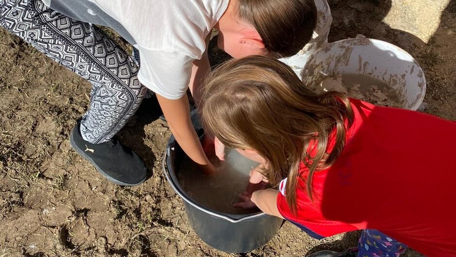 Children are bent over a bucket, wetting the clay