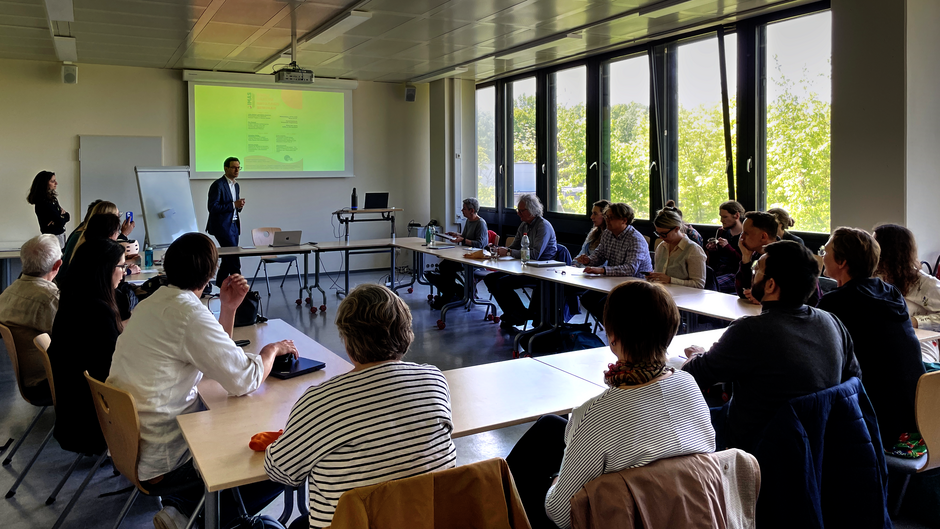 Seminarsaal, Vortragender, Menschen sitzen an Tischen (öffnet Vergrößerung des Bildes)