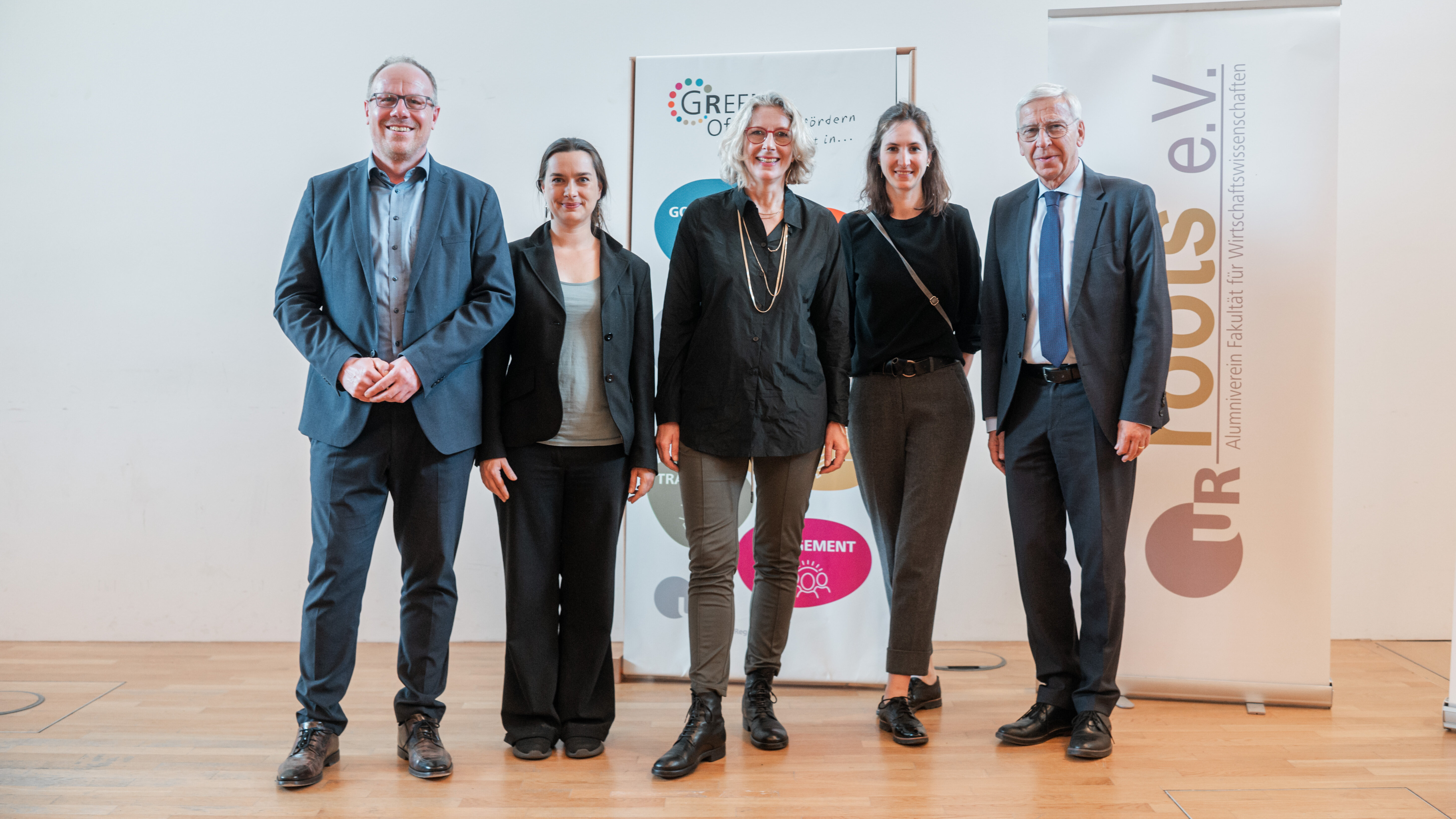 Gruppenfoto von zwei Männern und drei Frauen, die auf einer Bühne vor zwei Aufstellern stehen. Auf dem einen Aufsteller steht "Green Office" auf dem anderen Aufsteller steht "roots e.V.". (öffnet Vergrößerung des Bildes)