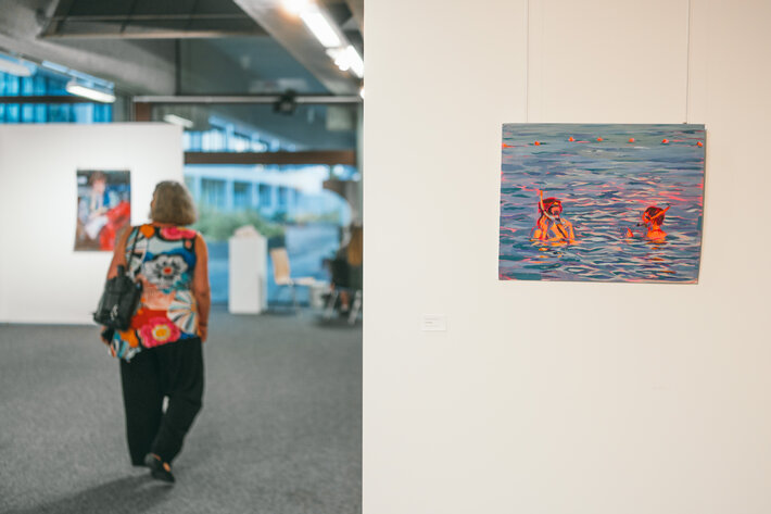 Eine Ausstellungsbesucherin geht durch die Stellwände. In der rechten Bildhälfte ist eine Zeichnung zu erkennen, auf der zwei junge Frauen mit Schnorchel schwimmen. (öffnet Vergrößerung des Bildes)