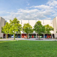 Blick über eine Wiese und Bäume auf den Gebäudeteil Philosophie/Theologie am Campus der Universität Regensburg