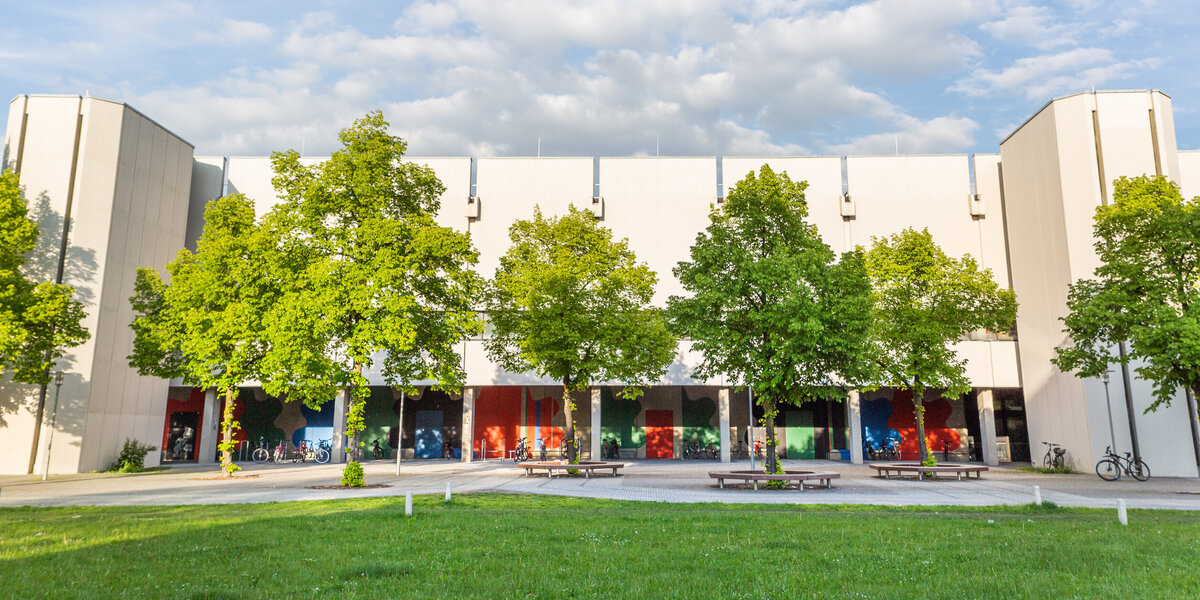 Blick über eine Wiese und Bäume auf den Gebäudeteil Philosophie/Theologie am Campus der Universität Regensburg