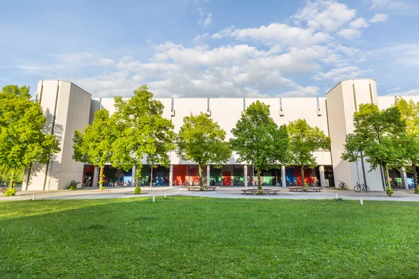 Blick über eine Wiese und Bäume auf den Gebäudeteil Philosophie/Theologie am Campus der Universität Regensburg