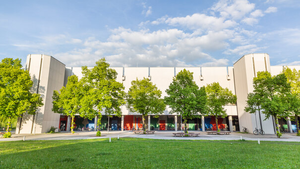 Blick über eine Wiese und Bäume auf den Gebäudeteil Philosophie/Theologie am Campus der Universität Regensburg