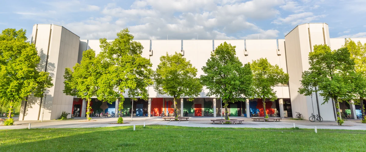 Blick über eine Wiese und Bäume auf den Gebäudeteil Philosophie/Theologie am Campus der Universität Regensburg