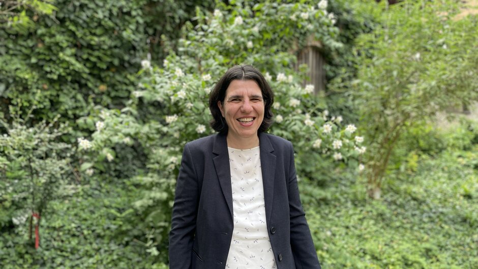 Stehende Frau vor grünen Bäumen und Büschen