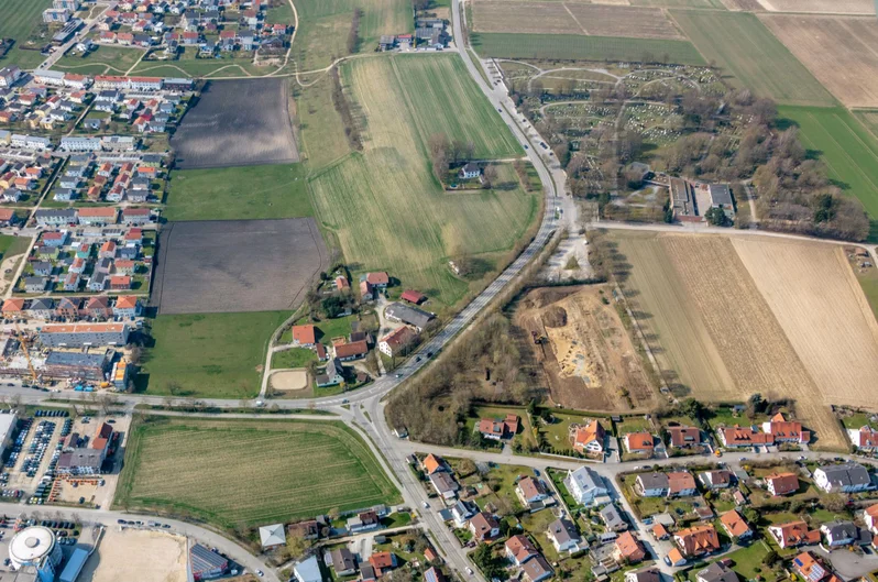 Luftbild einer modernen Wohnsiedlung, die von Feldern und breiteren Straßen durchrbochen wird. Rechts versetzt von der Bildmitte ist ein Grabungsareal zu erkennen. (öffnet Vergrößerung des Bildes)