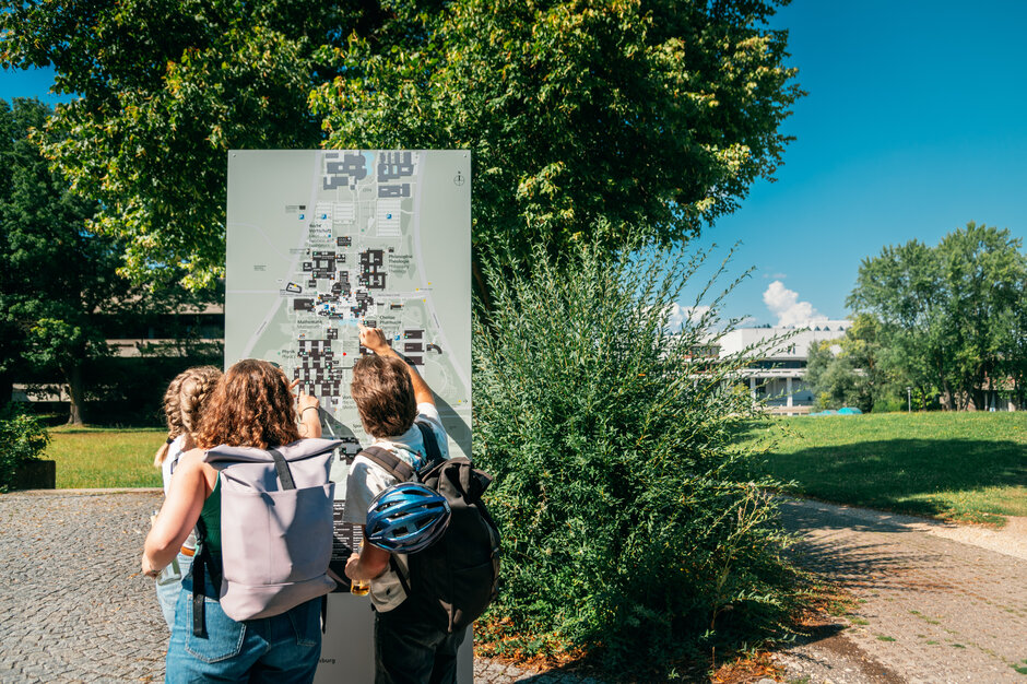 Studierende stehen gemeinsam vor einer Stele mit einem schematischen Lageplan der Universität Regensburg