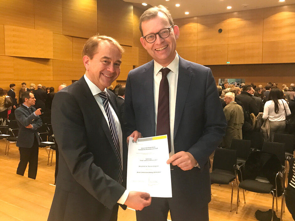 Prof. Maschmann überreicht Prof. Kingreen auf der Fakultätsfeier im vollbesetzten Hörsaal H24 die Urkunde. (öffnet Vergrößerung des Bildes)