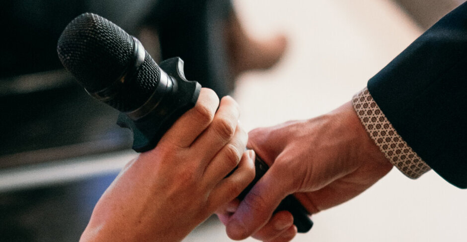 Ein Mikrofon wird von einer Hand zu einer anderen weitergereicht.