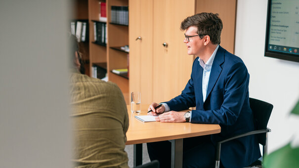 Ein Professor sitzt an einem Besprechungstisch und diskutiert mit seinen Mitarbeitern.