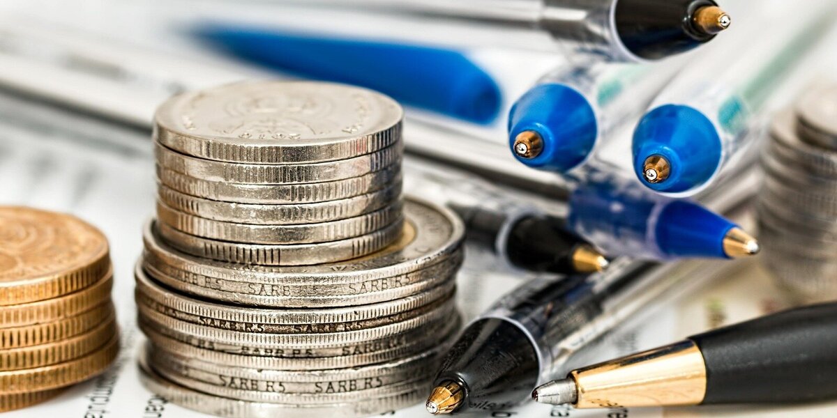 Münzstapel auf Formularblättern mit Stiften dazwischen liegend.