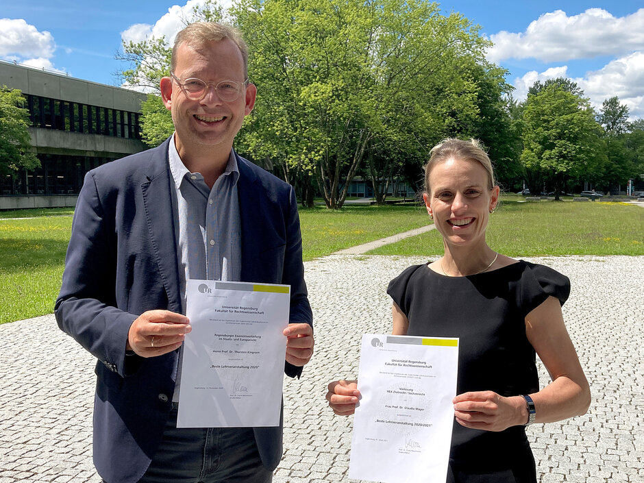 Frau Prof. Mayer überreicht Prof. Kingreen auf dem Freigelände vor dem Vielberthgebäude die Urkunde zum Lehrpreis. (öffnet Vergrößerung des Bildes)