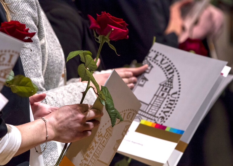 Absolventenfeier: Studierende halten Urkundenmappen im Design der Universität Regensburg und langstielige rote Rosen in den Händen. 