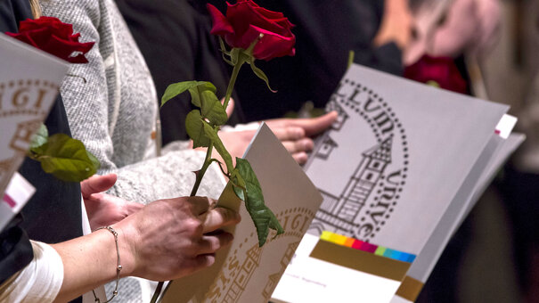 Absolventenfeier: Studierende halten Urkundenmappen im Design der Universität Regensburg und langstielige rote Rosen in den Händen. 