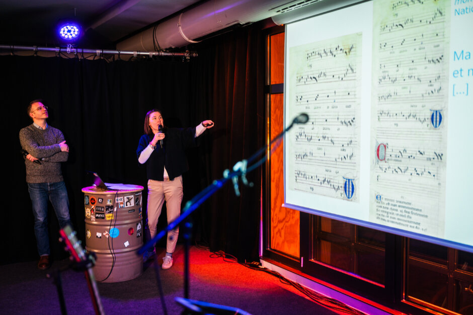 Ein Mann und eine Frau stehen auf einer Bühne und erklären die Projektion auf der Leinwand neben ihnen.