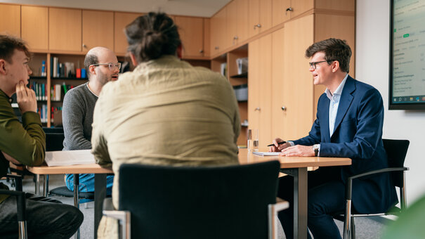 Vier Männer sitzen um einen Besprechungstisch in einem Büro und diskutieren.