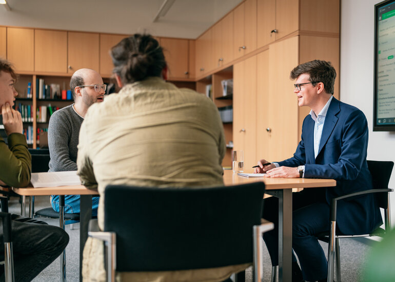 Vier Männer sitzen um einen Besprechungstisch in einem Büro und diskutieren.