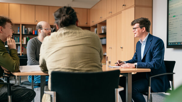 Vier Männer sitzen um einen Besprechungstisch in einem Büro und diskutieren.
