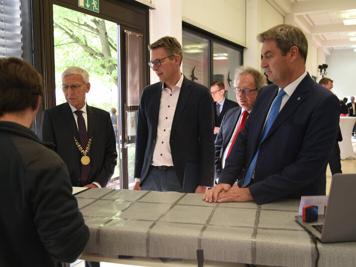 Mehrere Personen stehen an einem hohen Tisch und blicken in Richtung eines aufgeklappten Laptops (öffnet Vergrößerung des Bildes)