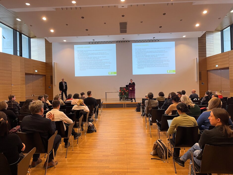 Voller Hörsaal, sitzendes Publikum schaut auf stehende Rednerin, dahinter an der Wand Powerpoint-Folien. (öffnet Vergrößerung des Bildes)