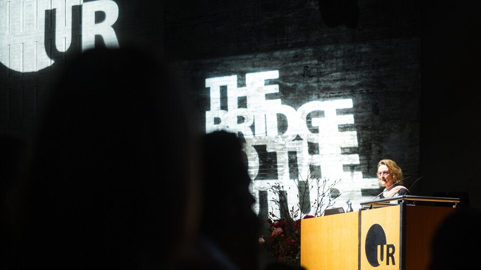 Frau mit Brille an Redepult, im Hintergrund Schriftzug "The Bridge to the Future"