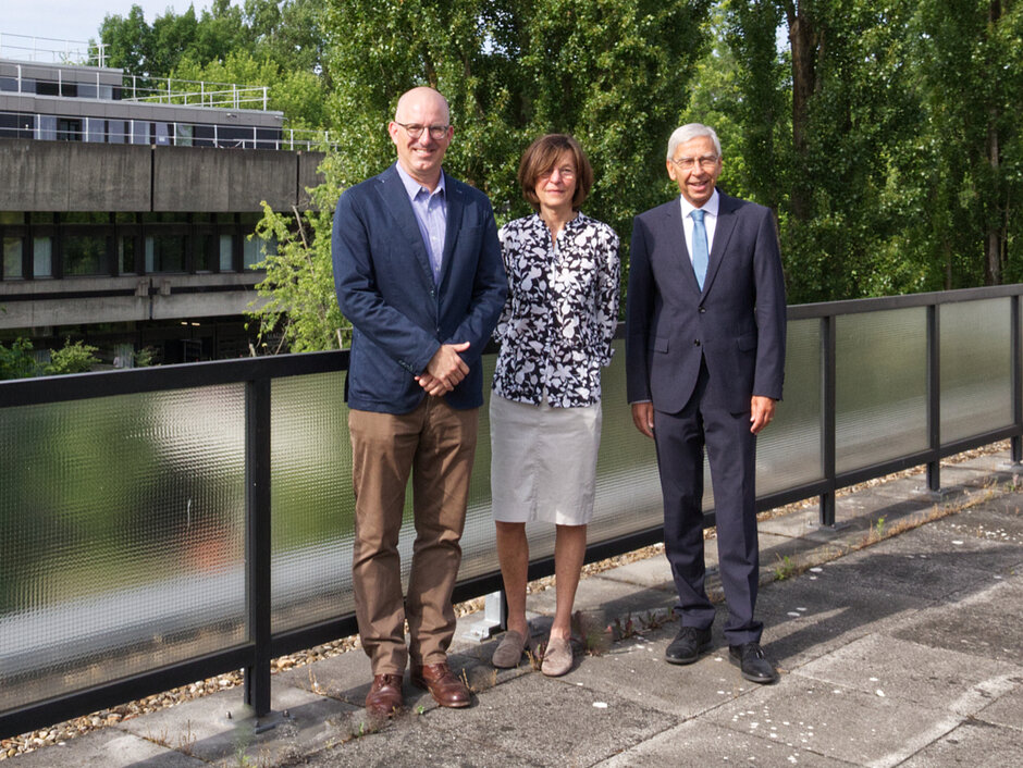 Drei Personen haben sich für ein Gruppenbild auf einer Dachterasse aufgestellt.