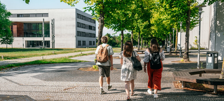 Eine Gruppe Studierender geht auf das Vielberth-Gebäude am Campus der Universität Regensburg zu.