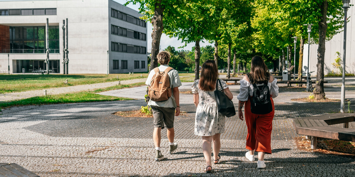 Eine Gruppe Studierender geht auf das Vielberth-Gebäude am Campus der Universität Regensburg zu.