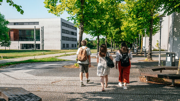 Eine Gruppe Studierender geht auf das Vielberth-Gebäude am Campus der Universität Regensburg zu.