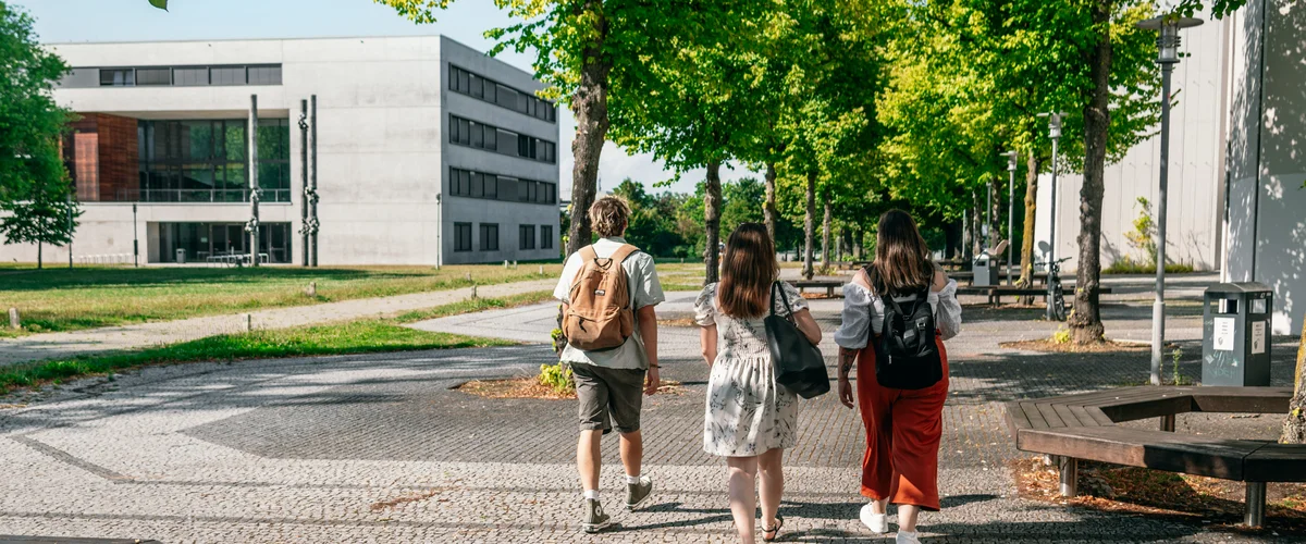 Eine Gruppe Studierender geht auf das Vielberth-Gebäude am Campus der Universität Regensburg zu.