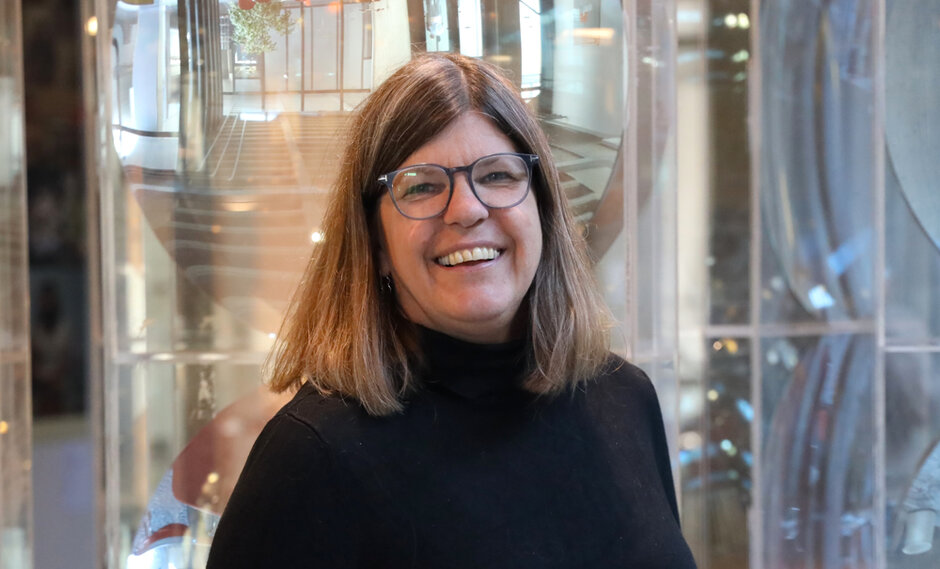 Eine Frau mit Brille und schwarzem Rollkragenpullover blickt lächelnd zum Betrachter