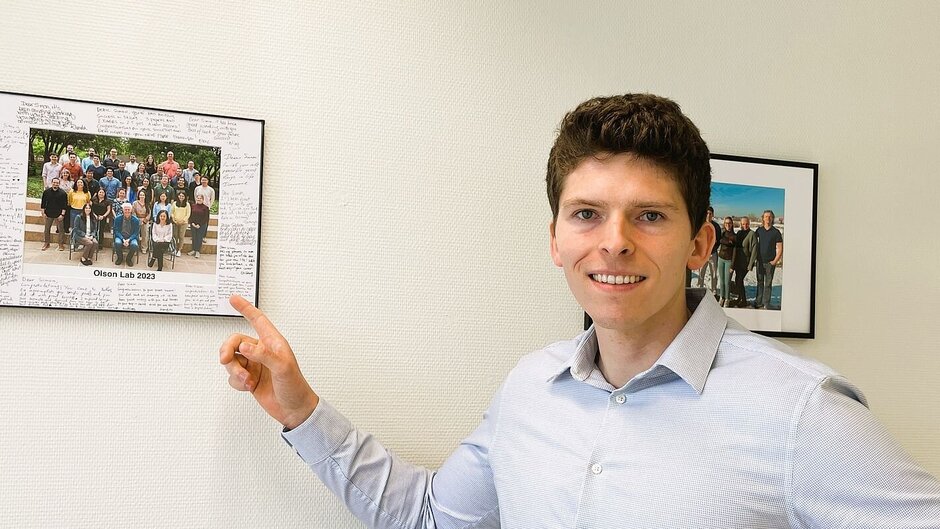 Lächelnder Mann deutet auf an der Wand hängendes Gruppenbild.