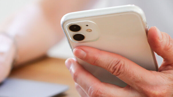 Eine Person hält ein Smartphone in der Hand und tippt etwas am Laptop.