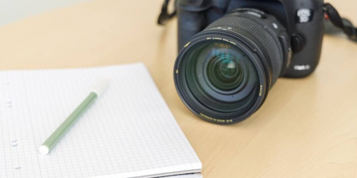 Spiegelreflexkamera und Block liegen auf einem Tisch.