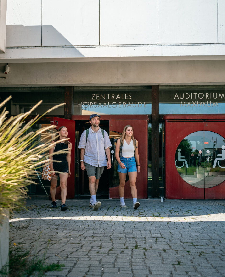 Drei Studierende verlassen das Zentrale Hörsaalgebäude der Universität Regensburg.