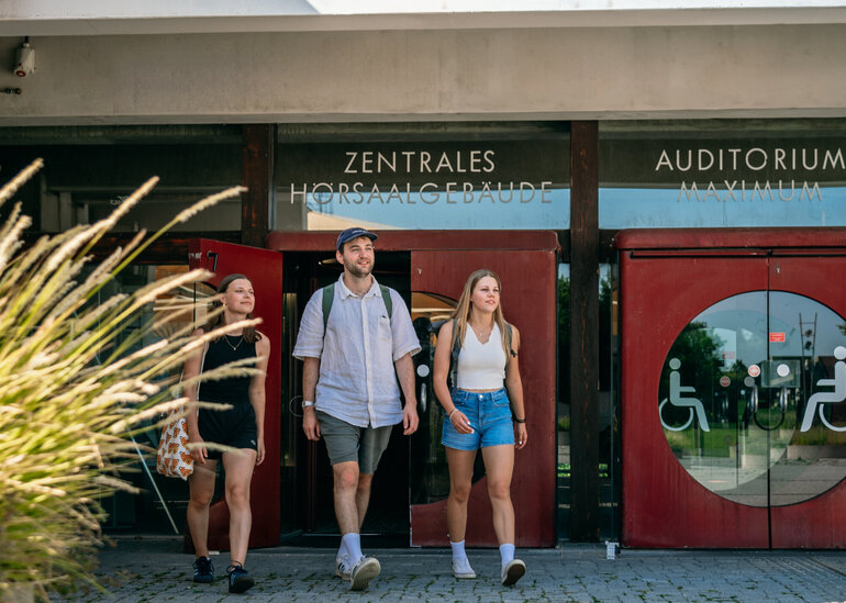 Drei Studierende verlassen das Zentrale Hörsaalgebäude der Universität Regensburg.