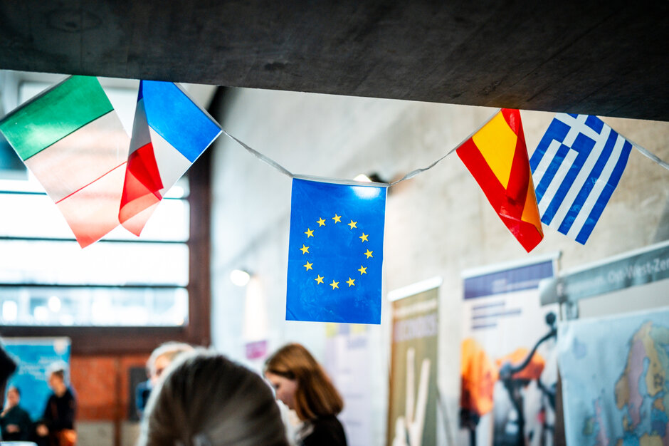 Miniaturflaggen von Italien, Frankreich, Spanien, Griechenland und der EU hängen als Wimpelkette an einem Infostand